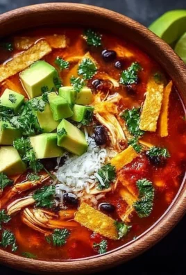 A bowl of delicious chicken tortilla soup topped with crispy tortilla strips and avocado.